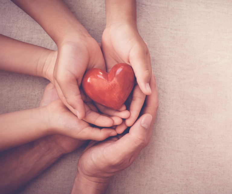 Man, woman and child's hands holding a red wooden heart gently