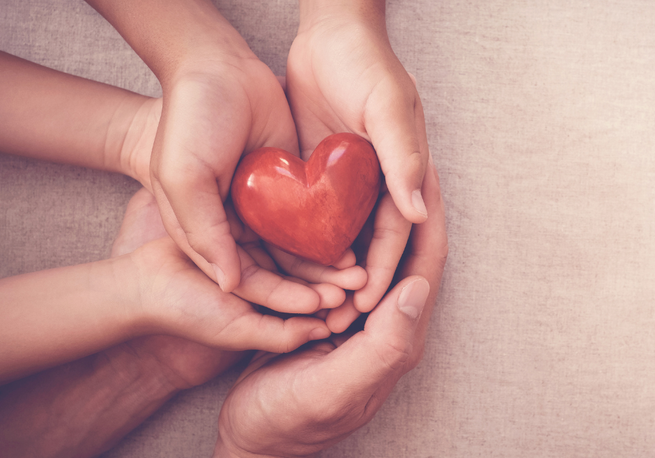 Man, woman and child's hands holding a red wooden heart gently