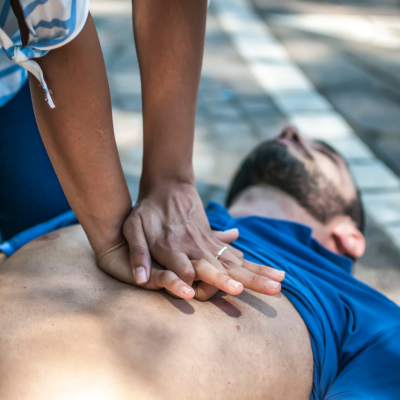 Woman performing CPR first aid on unconscious man on the ground